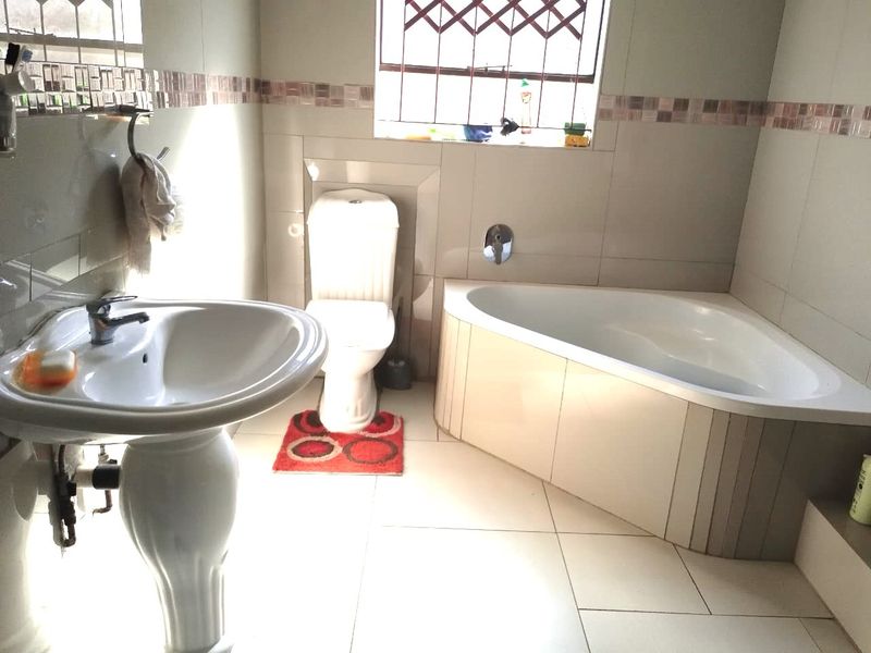 A functional bathroom featuring a corner bathtub, pedestal basin, and toilet with neutral wall and floor tiling.