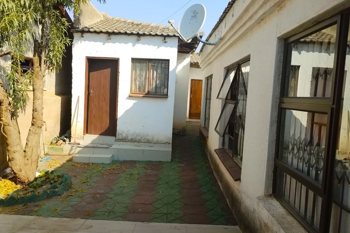 A view of the rear exterior area featuring paved pathways, tiled roofing, and access to multiple entry points of the property.