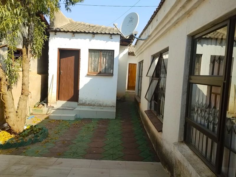 A view of the rear exterior area featuring paved pathways, tiled roofing, and access to multiple entry points of the property.