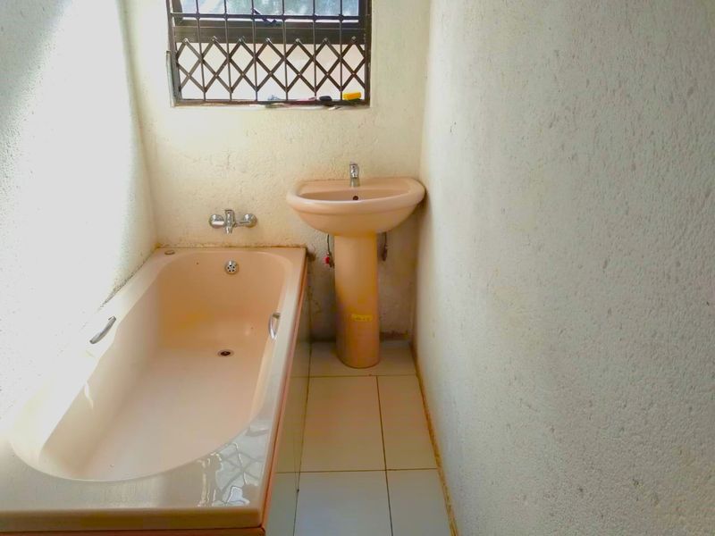 A dated bathroom featuring a peach-colored pedestal basin and matching bathtub, tiled flooring, and a window with security bars.