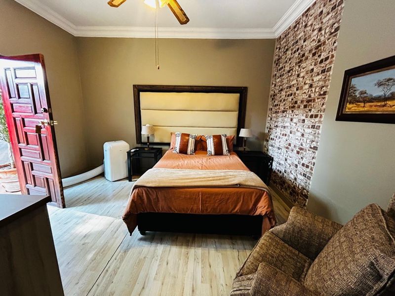 A bedroom featuring a brick-style feature wall, light wood-look flooring, and a ceiling fan, with direct access to an outdoor area.