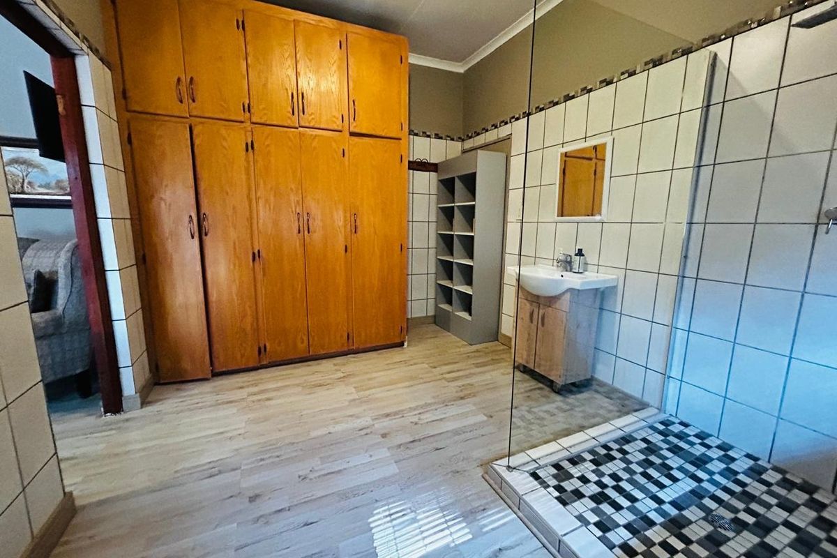 A functional bathroom featuring a glass-enclosed shower with decorative mosaic floor tiles, a pedestal vanity, and extensive built-in wooden storage cabinetry.