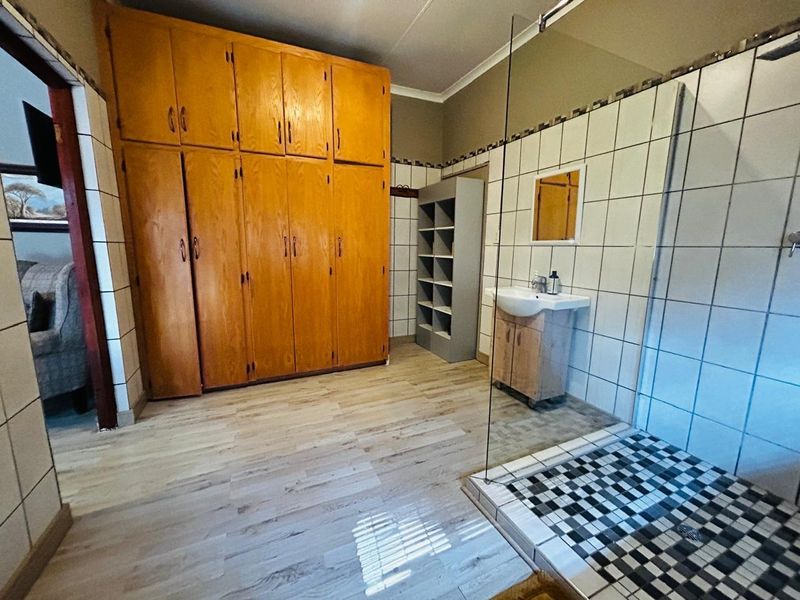 A functional bathroom featuring a glass-enclosed shower with decorative mosaic floor tiles, a pedestal vanity, and extensive built-in wooden storage cabinetry.