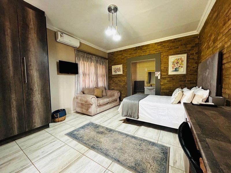 A well-maintained bedroom featuring exposed brick feature walls, tiled flooring, built-in cabinetry, and an en-suite bathroom access.