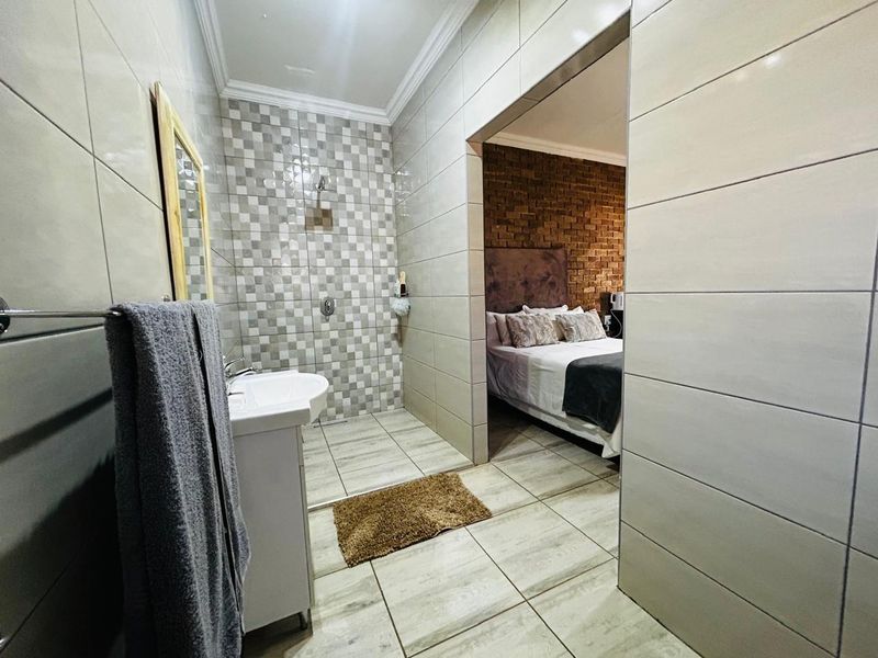 A modern bathroom featuring tiled walls and a walk-in shower, with an open-plan transition into the adjacent bedroom area.