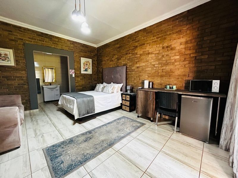 A bedroom featuring exposed brick walls, tiled flooring, and an en-suite bathroom with a vanity unit.