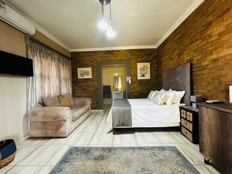A spacious bedroom featuring exposed brick feature walls, tiled flooring, and an en-suite bathroom access point.