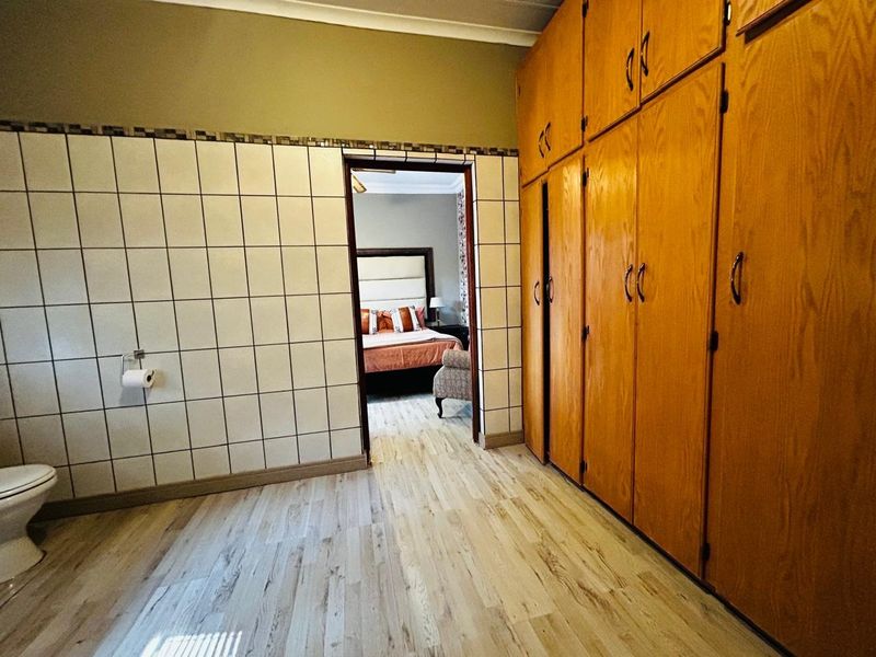 A dressing area featuring extensive built-in wooden cabinetry, tiled wall accents, and wood-look flooring, providing direct access to the adjacent bedroom.