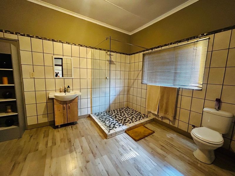 A functional bathroom featuring a walk-in glass shower, pedestal vanity, and toilet, finished with neutral wall tiling and wood-look flooring.