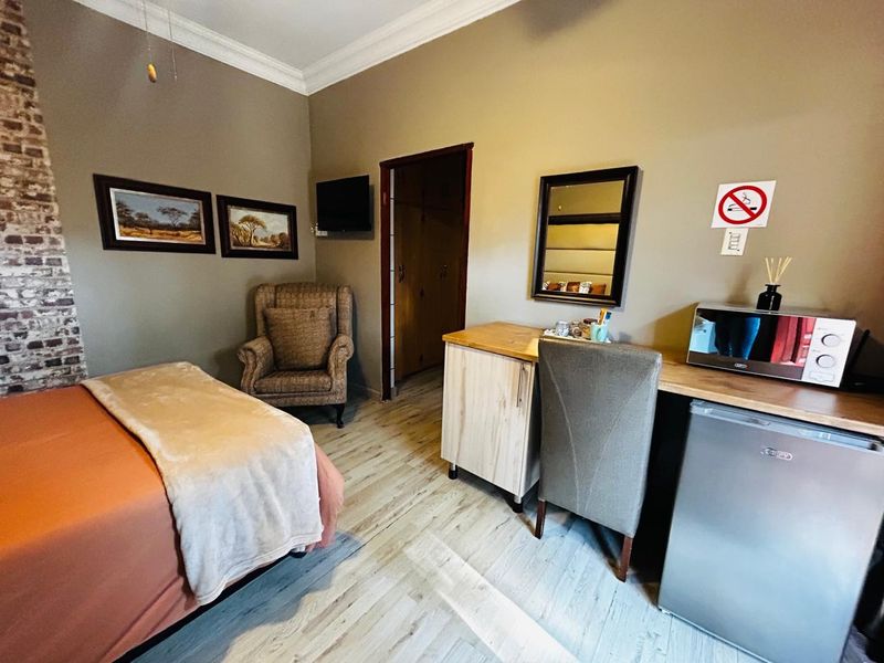A bedroom featuring wood-look flooring, a brick accent wall, crown molding, and a built-in doorway leading to an adjacent space.