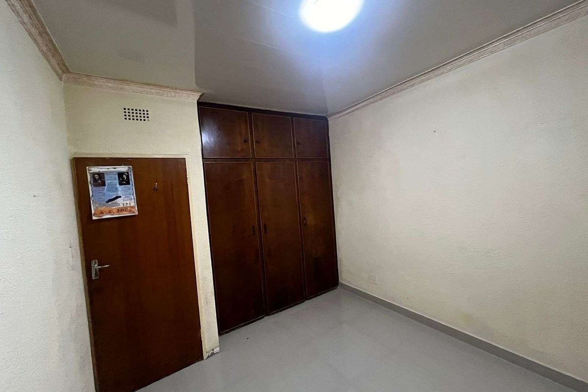 A bedroom featuring built-in wooden cupboards, a glossy ceiling finish, and tiled flooring, providing a functional and neutral living space.