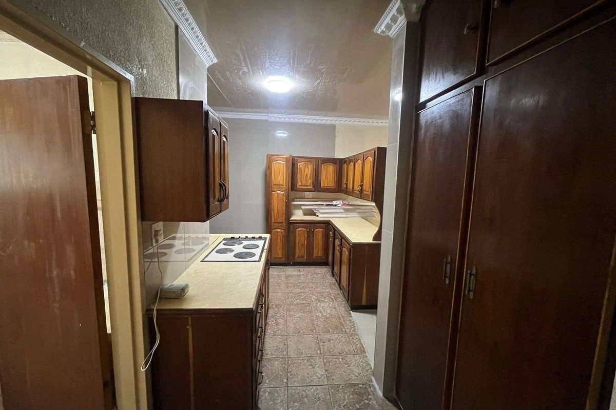A dated kitchen featuring dark wood cabinetry, built-in hob, and tiled flooring, offering a functional layout with significant potential for modernization and renovation.