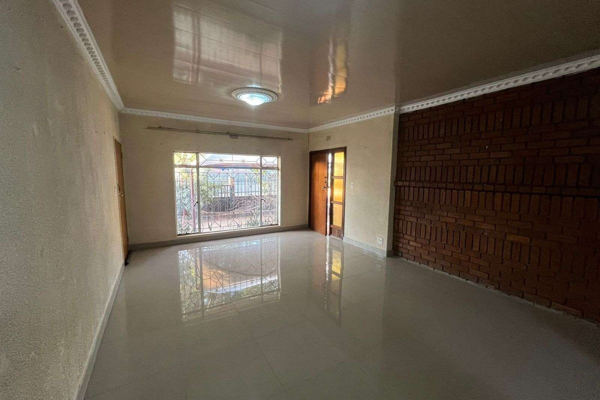 Spacious living area featuring polished tile flooring, a prominent exposed brick feature wall, and large windows with security bars.