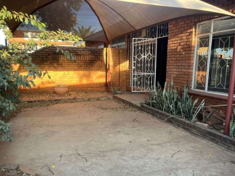 A paved outdoor patio area featuring a shade sail, brick boundary wall, and security gate access to the main townhouse structure.