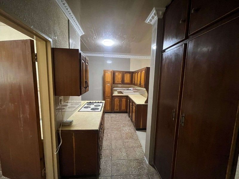 A dated kitchen featuring dark wood cabinetry, built-in hob, and tiled flooring, offering a functional layout with significant potential for modernization and renovation.