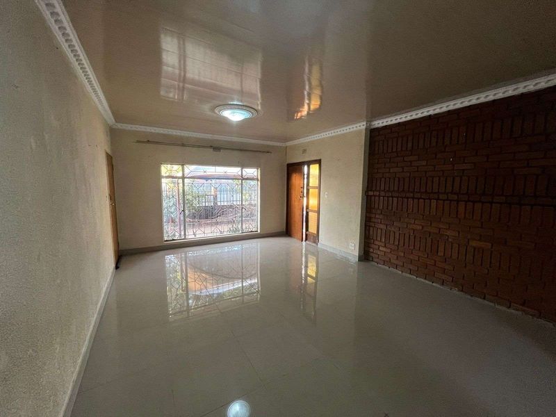 Spacious living area featuring polished tile flooring, a prominent exposed brick feature wall, and large windows with security bars.