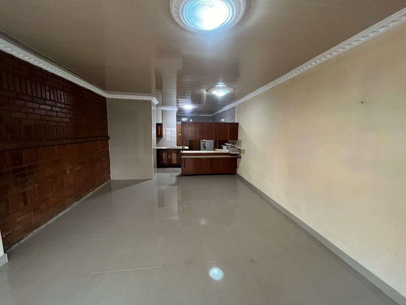An open-plan living and kitchen area featuring tiled flooring, a brick feature wall, and built-in wooden cabinetry.