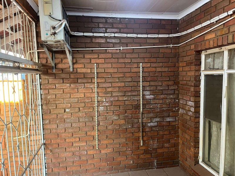 A utility area featuring exposed brick walls, surface-mounted electrical conduit, and a wall-mounted air conditioning unit.