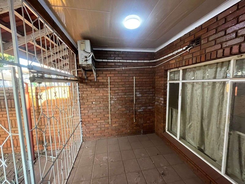 A covered patio area featuring exposed brick walls, tiled flooring, and a security gate, suitable for outdoor utility or storage use.