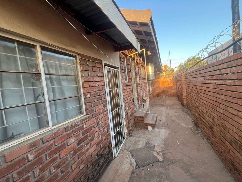 A narrow exterior side passage featuring exposed brick walls, concrete paving, and metal security gates, providing access to the rear of the townhouse.