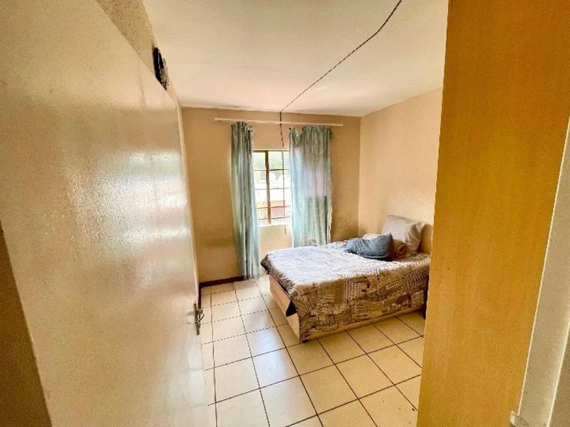 A bedroom featuring tiled flooring and a window, showing signs of wear on the walls and ceiling.