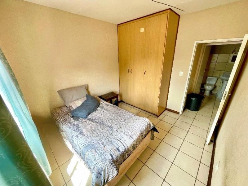 A bedroom featuring tiled flooring and a built-in wardrobe, with an adjoining bathroom visible through the doorway.