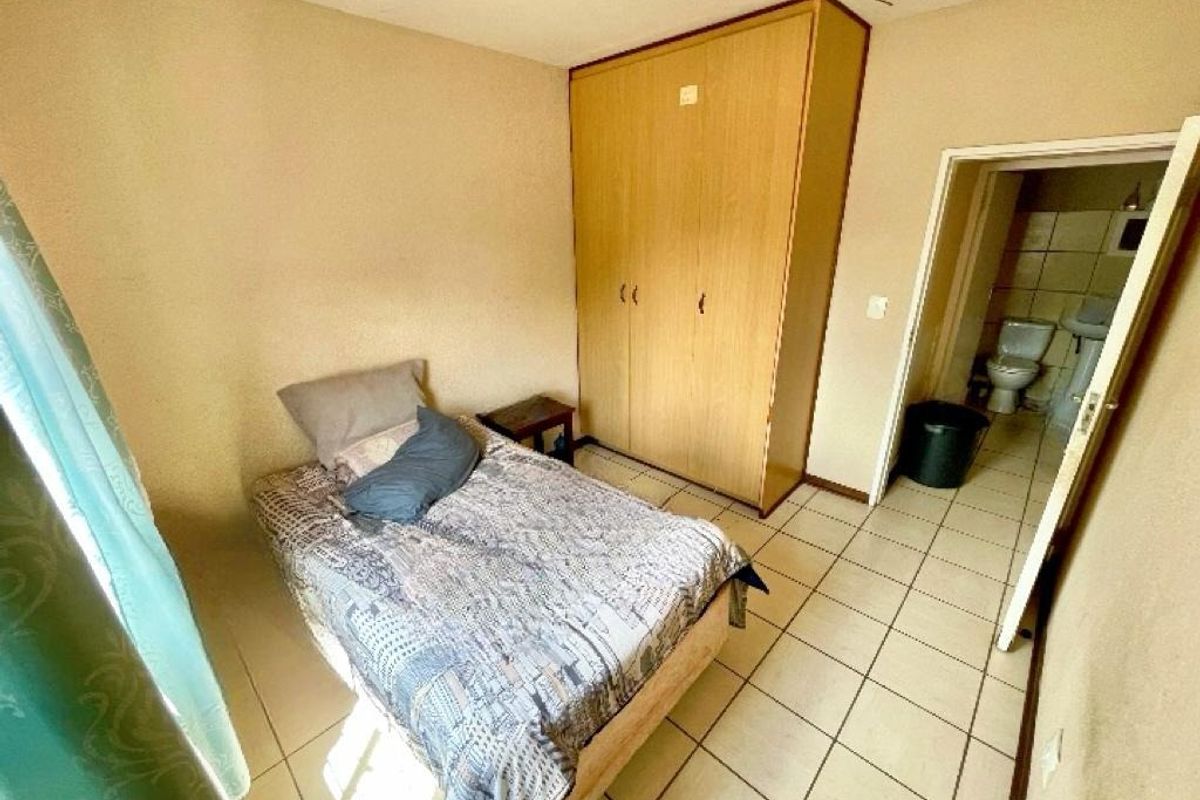 A bedroom featuring tiled flooring and a built-in wardrobe, with an adjoining bathroom visible through the doorway.