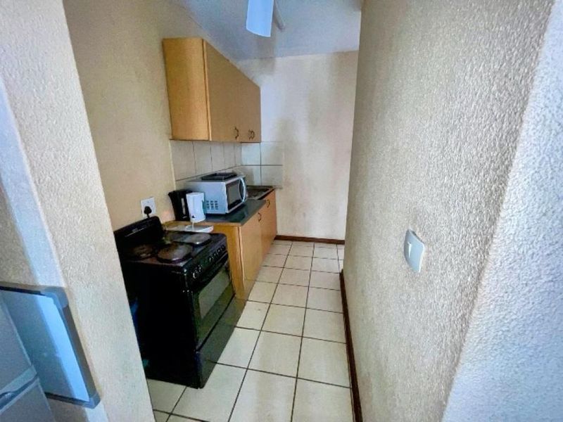 A compact, dated kitchen featuring tiled flooring, a tiled backsplash, and basic built-in cabinetry with a freestanding stove.