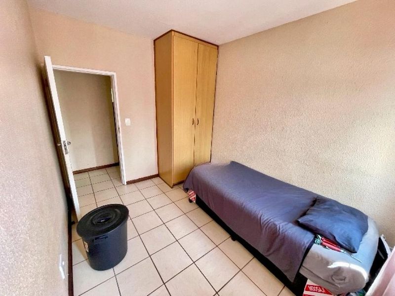 A simple bedroom featuring tiled flooring and a built-in wooden wardrobe, providing functional storage space.