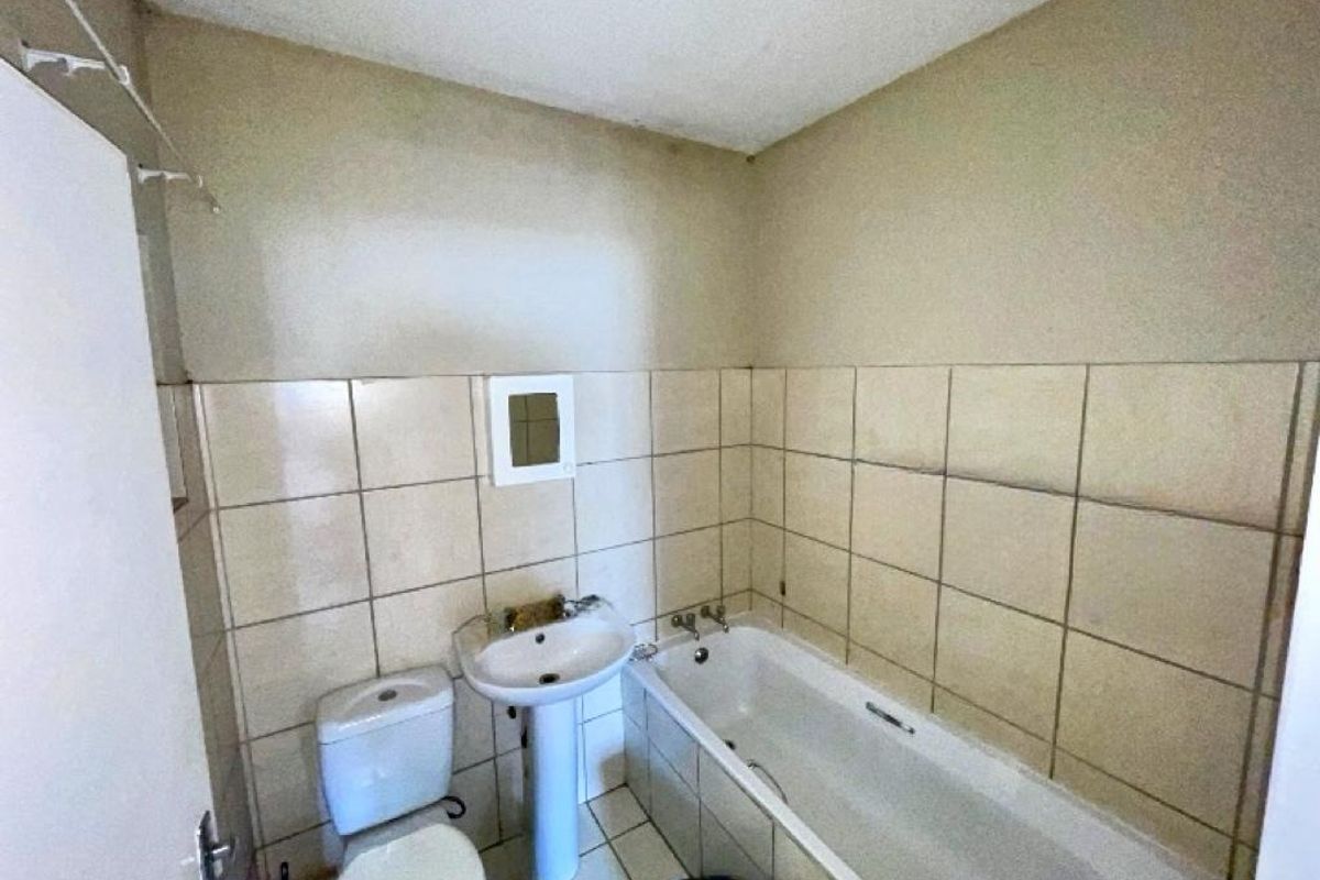 A dated bathroom featuring a pedestal basin, toilet, and bathtub with tiled walls and flooring, requiring cosmetic updates and maintenance.