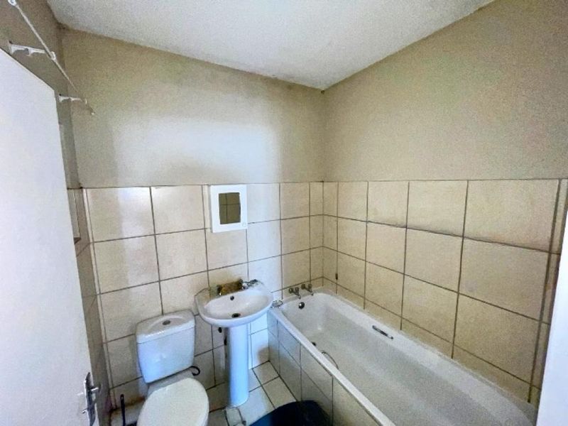 A dated bathroom featuring a pedestal basin, toilet, and bathtub with tiled walls and flooring, requiring cosmetic updates and maintenance.