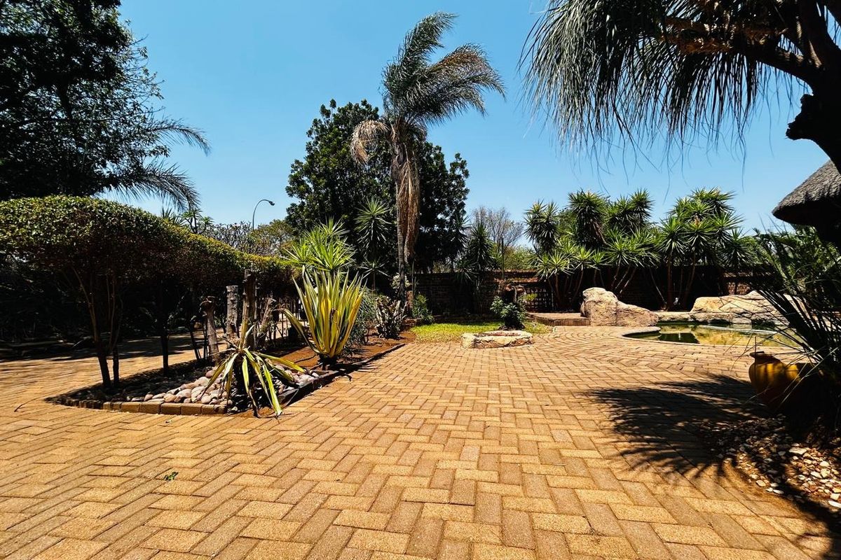 A well-maintained outdoor pool area featuring extensive brick paving, mature landscaping, and a stone-accented swimming pool.