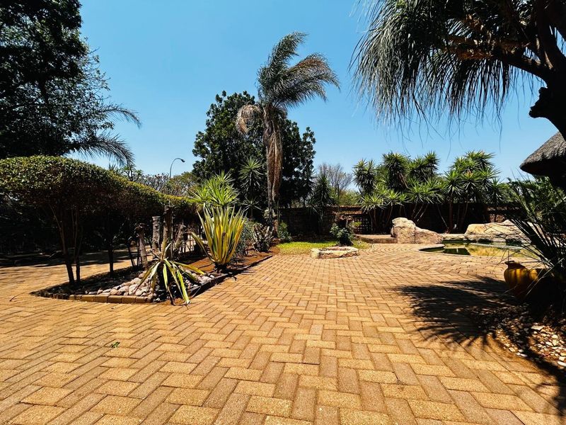 A well-maintained outdoor pool area featuring extensive brick paving, mature landscaping, and a stone-accented swimming pool.