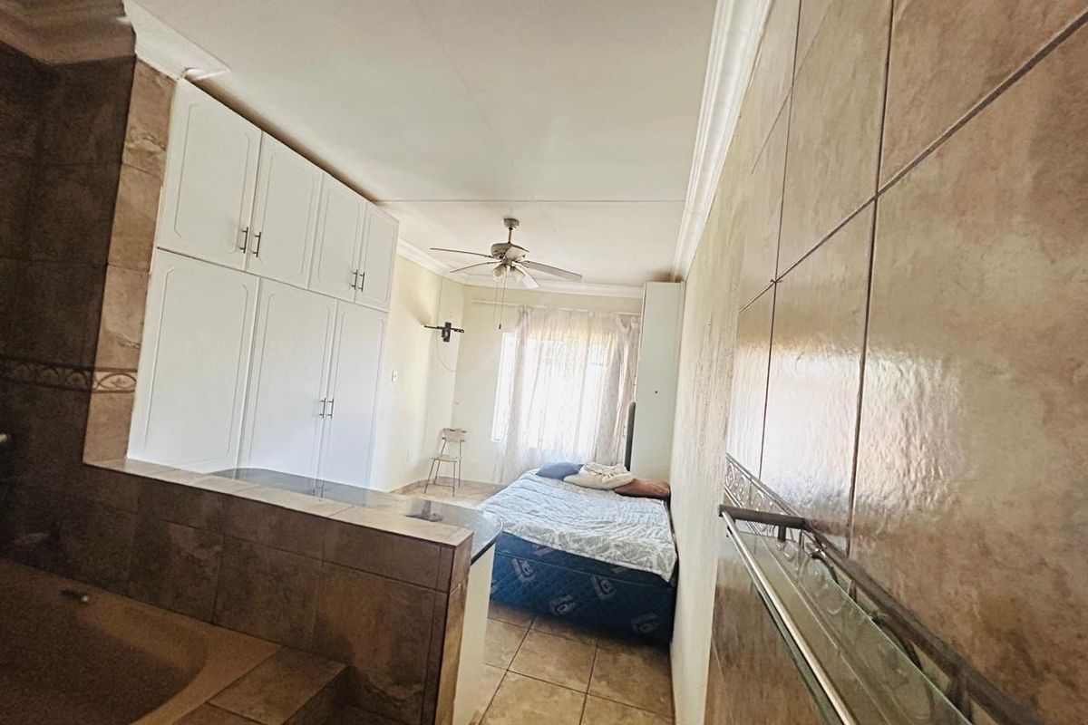 A bedroom featuring built-in cupboards, tiled flooring, and wall tiling, with a ceiling fan and integrated storage space.