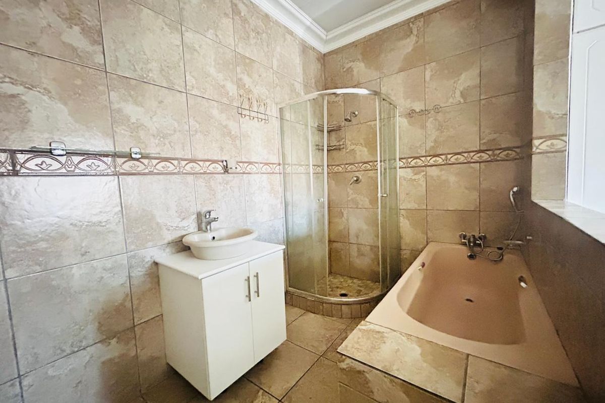 A functional bathroom featuring a corner shower enclosure, a built-in bathtub, and a vanity cabinet with a vessel sink, finished with neutral wall tiles.