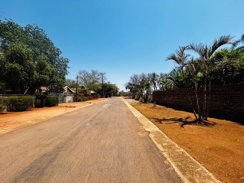 A view of the residential street approach, featuring an asphalt road, concrete curbing, and established brick boundary walls.