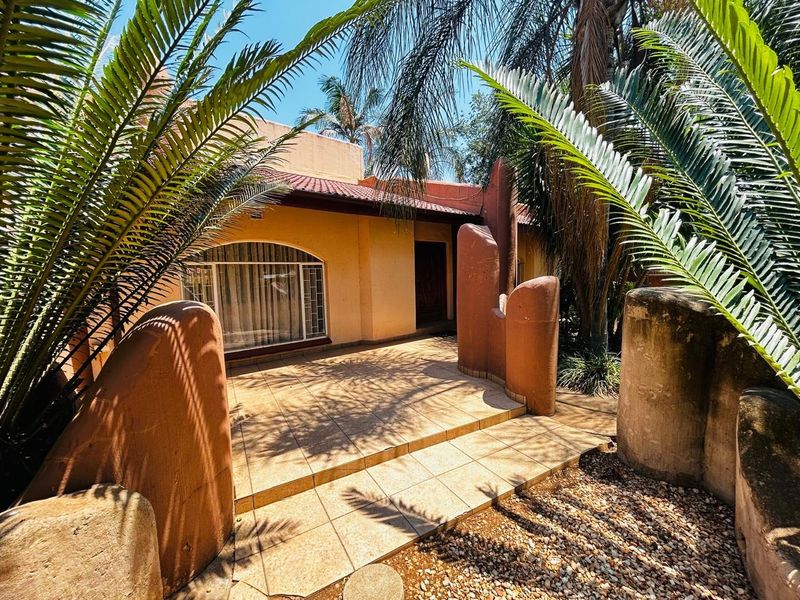 Front entrance area featuring a tiled patio, unique sculptural masonry pillars, and an arched window set against a stucco facade.