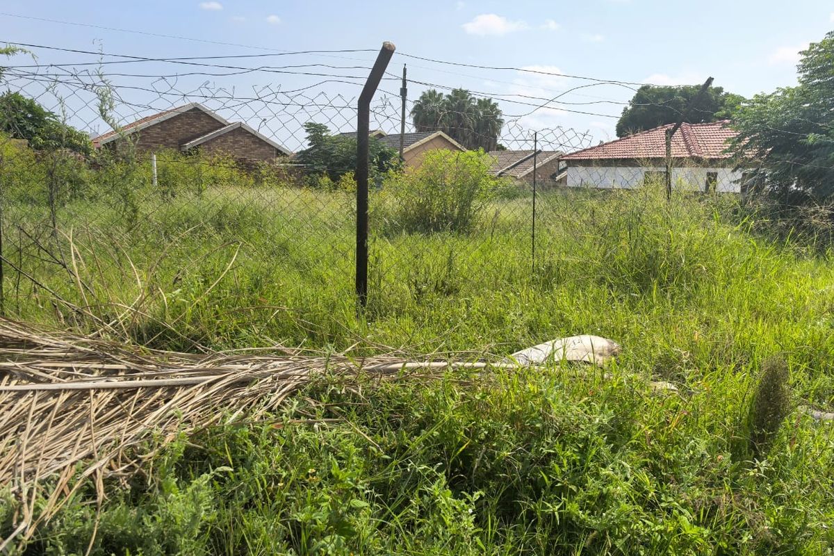 A view of a vacant residential plot featuring overgrown grass and existing wire mesh perimeter fencing.