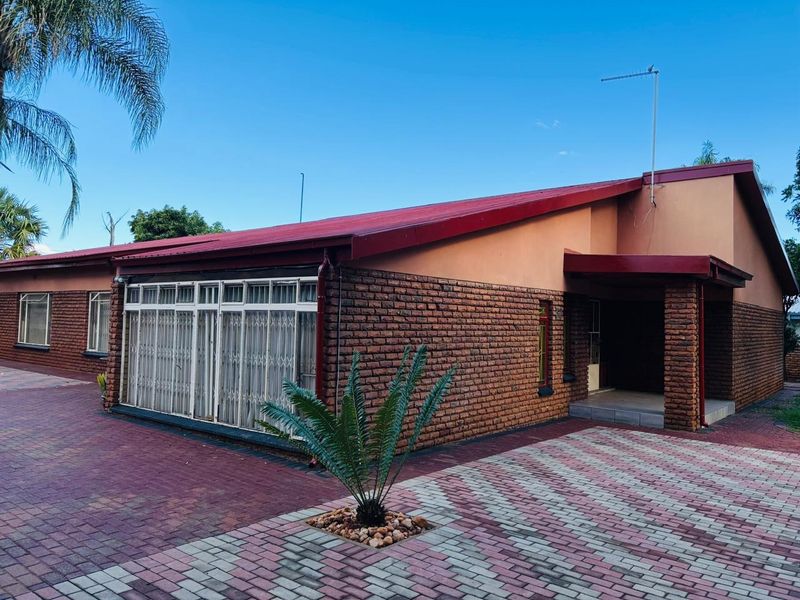 Front exterior view of a single-story brick house featuring a metal roof, paved driveway, and secure entrance area.