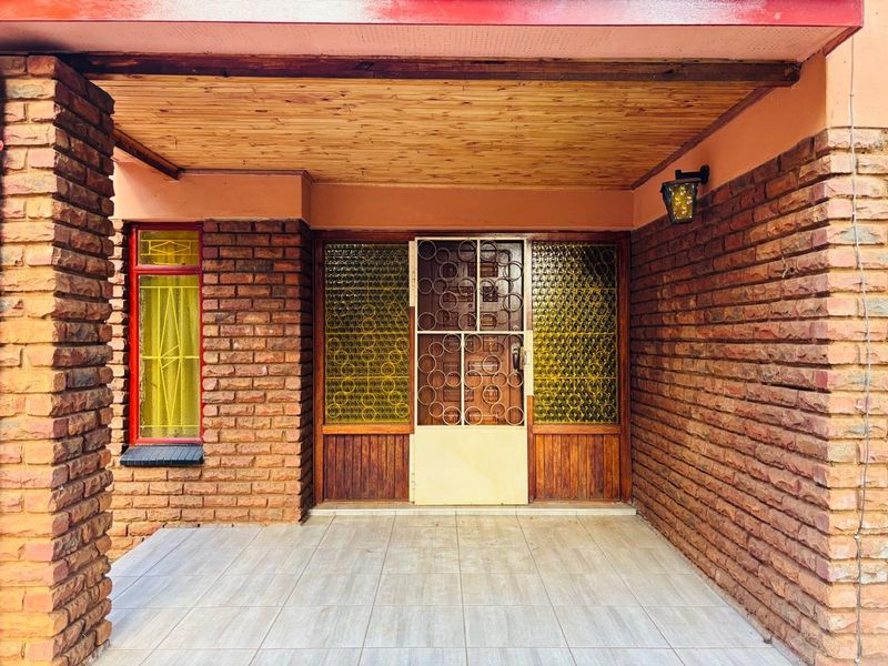 A covered entrance patio featuring exposed brick walls, a timber-clad ceiling, and tiled flooring, providing a sheltered transition to the home's main entrance.