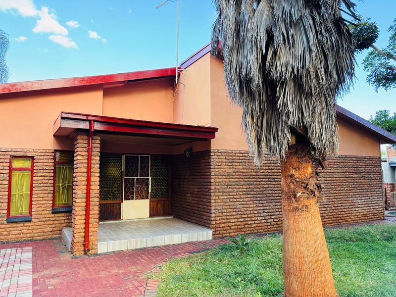 Front elevation of a brick house featuring a covered entrance porch, paved walkway, and established garden area.