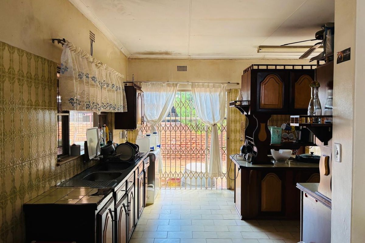 A dated kitchen featuring traditional cabinetry, tiled splashbacks, and direct access to the rear exterior through a security gate.