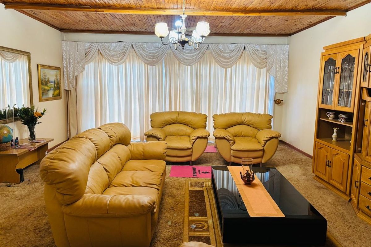 A traditional living room featuring a warm timber tongue and groove ceiling, a central chandelier, and a built-in wooden display cabinet.