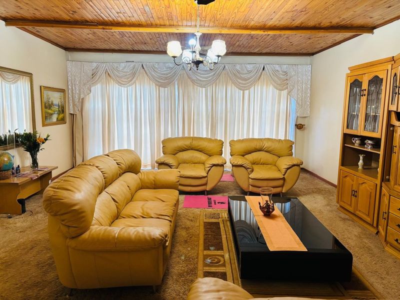 A traditional living room featuring a warm timber tongue and groove ceiling, a central chandelier, and a built-in wooden display cabinet.