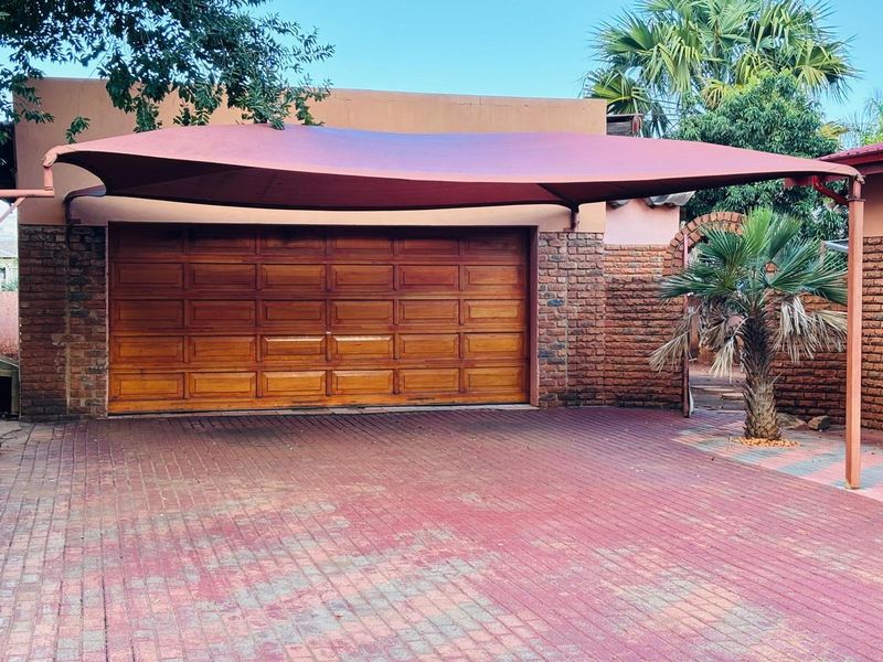 A well-maintained garage featuring a wooden sectional door, brick exterior walls, and a protective shade sail over the paved driveway area.
