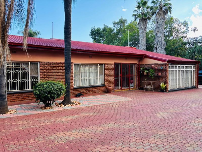 Rear view of a single-story brick house featuring a red metal roof, security gates, and an extensive paved courtyard area.