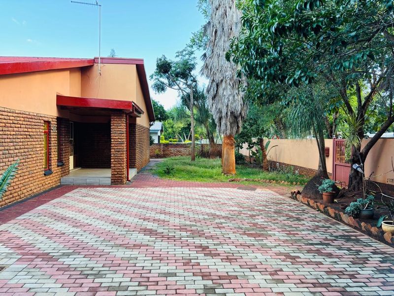 Front exterior view of the house featuring a paved driveway, covered entrance, and established garden area with boundary walling.