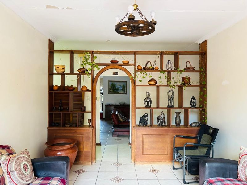 Living room featuring a prominent built-in wooden room divider with an arched opening, ceramic tiled flooring, and a rustic wagon wheel ceiling light.
