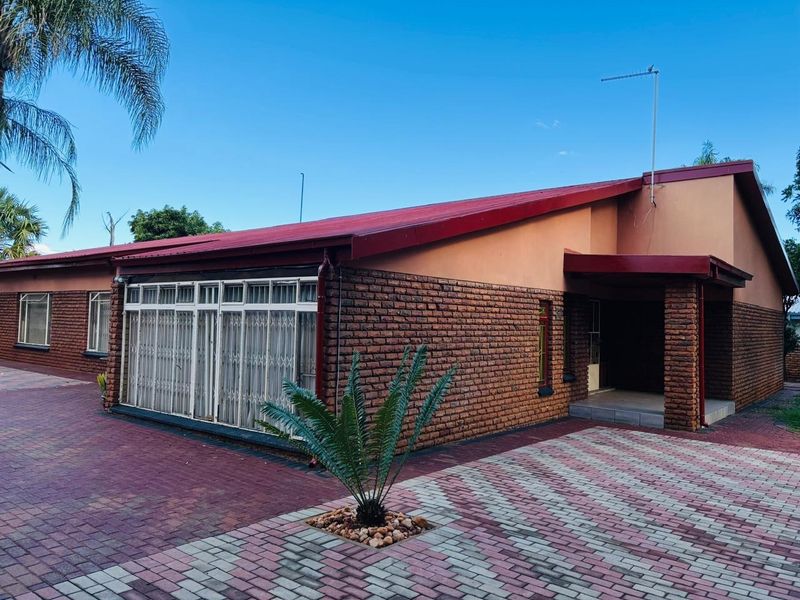 Front exterior view of a single-story brick house featuring a metal roof, paved driveway, and secure entrance area.