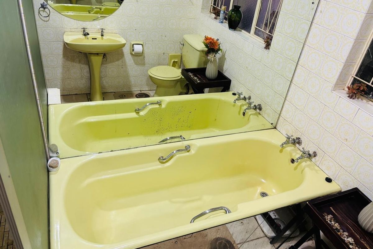 A dated bathroom featuring original yellow sanitaryware, including a pedestal basin, toilet, and bathtub, with tiled walls and flooring.